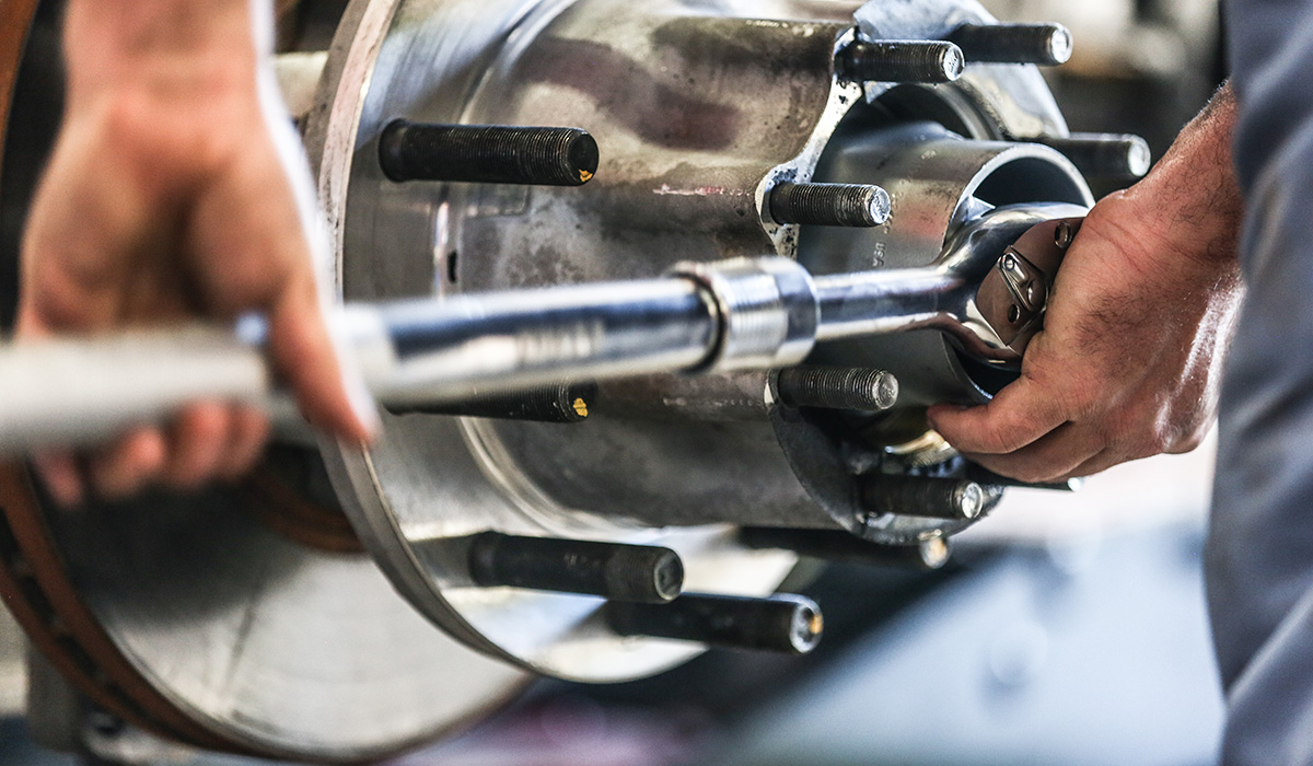 Close up photo of technician working on truck brakes with wrench.